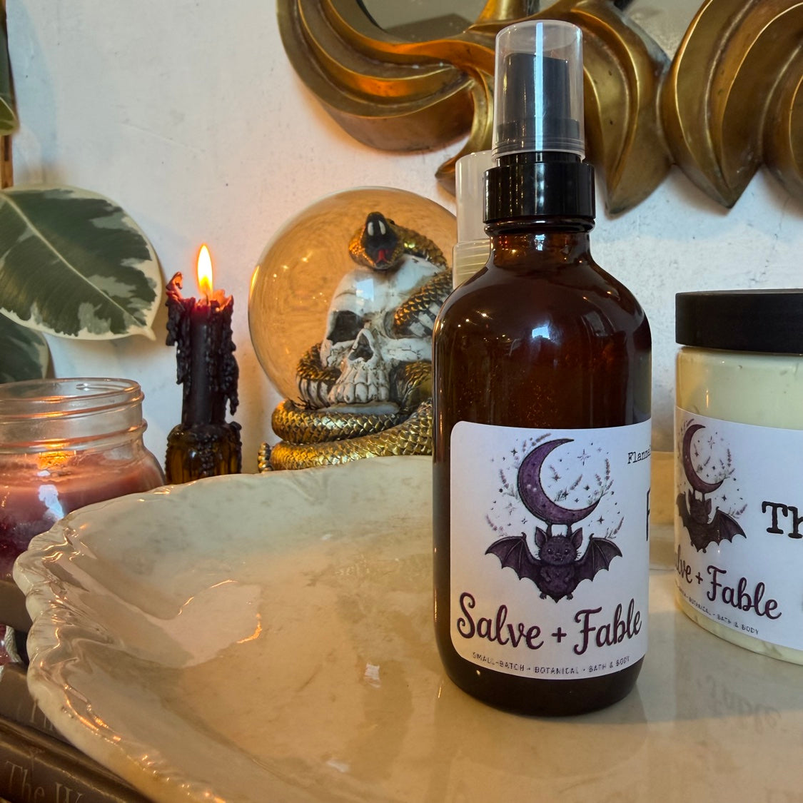 Flannel + Fable XL magnesium spray bottle with Salve + Fable storybook bat label, styled with candles and a skull snow globe