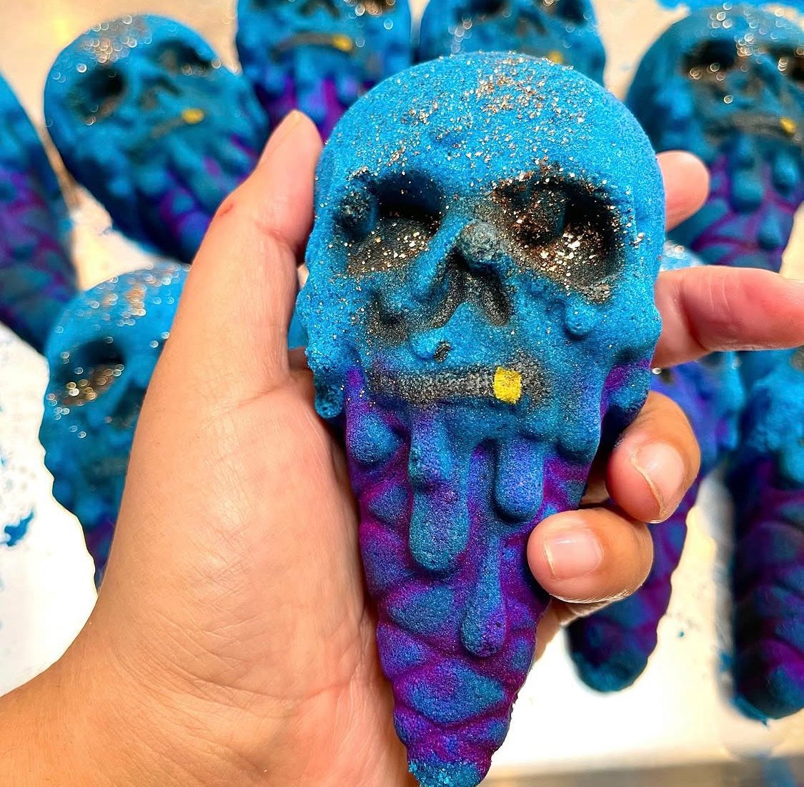Berrycide bath bomb held in hand, blue skull with gold tooth over a purple cone