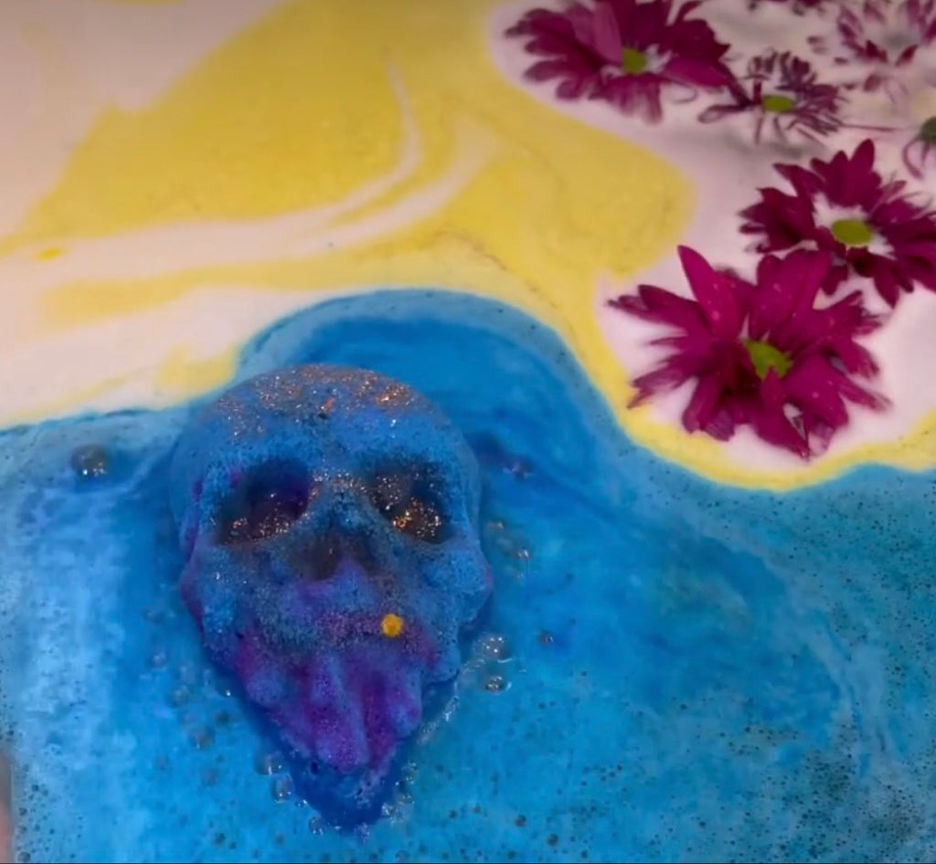 Berrycide bath bomb fizzing in blue bath water with magenta flowers