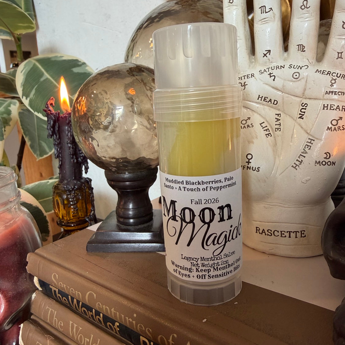 Moon Magick Legacy Menthol Salve stick, label front, styled with palmistry hand and crystal ball