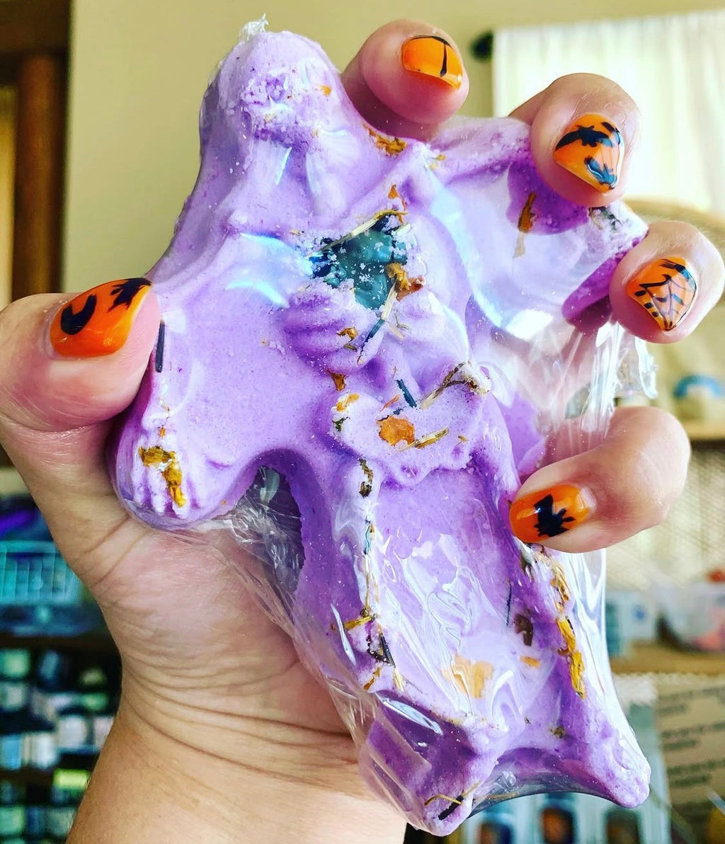 Spooky Scary Skeletons bath bomb held in hand, wrapped, showing the lavender skeleton shape