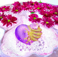 VooDoo Queen Valentine bath bomb, a purple heart with gold ribcage detail, fizzing among magenta flowers